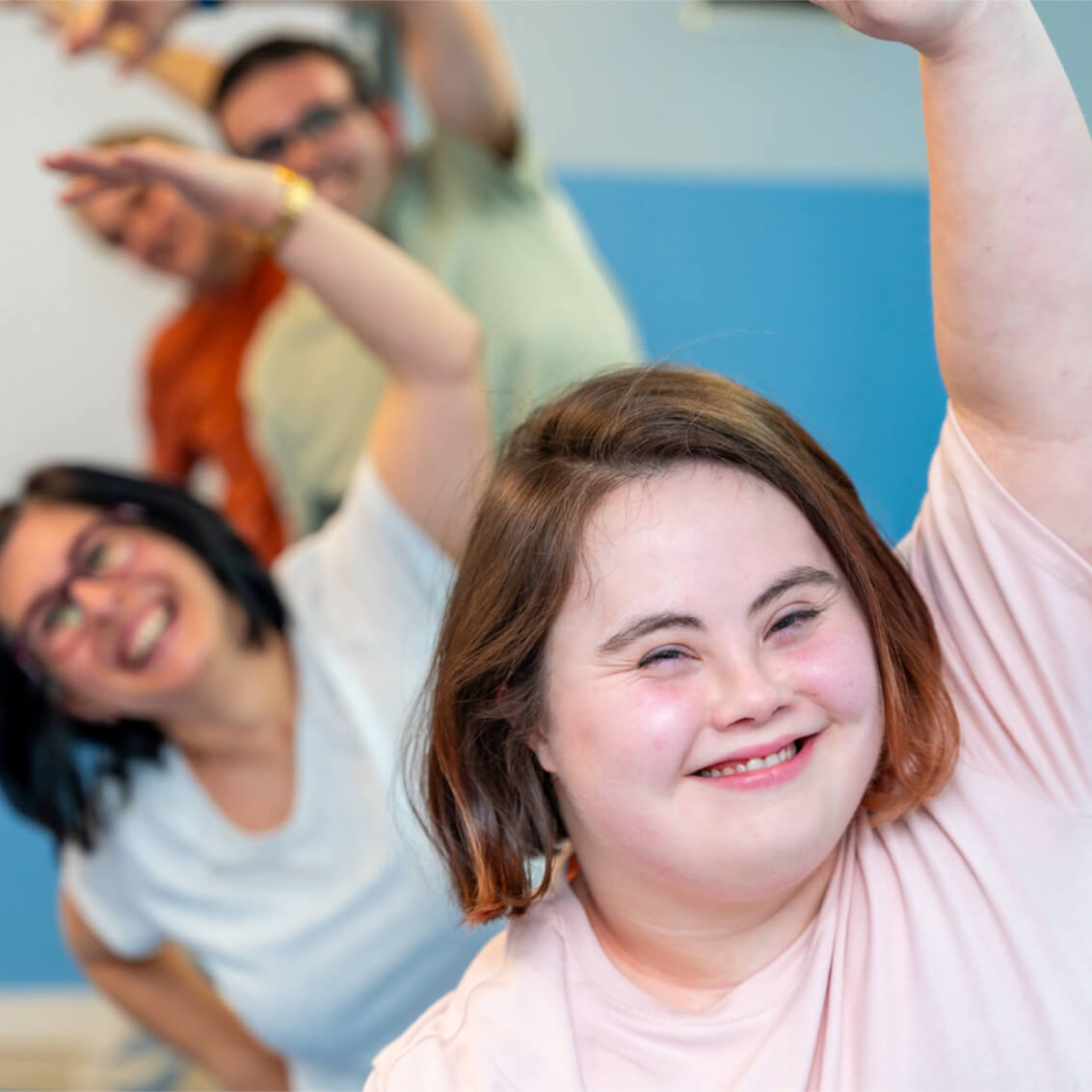 A young woman with Down's syndrome smiles broadly while taking part in an aerobics class.