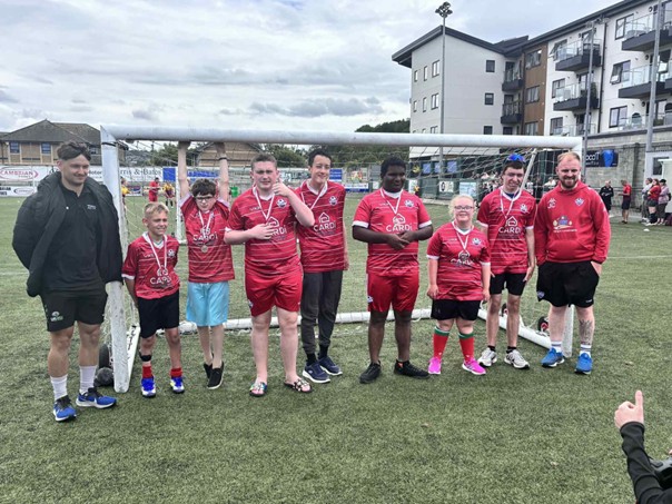 Llechrys Dragons members pose for a photo. Team members and their coach are lined up on a n outdoor football field, standing in front of the goal.