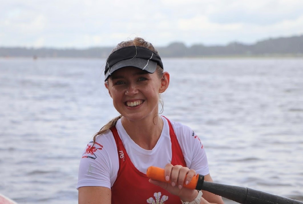 Rebekah in her Welsh Rowing kit, afloat and holding an oar. She is looking at the camera and smiling.