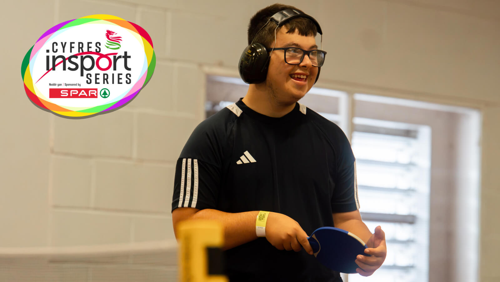 A young man wearing ear defenders is smiling while playing para table tennis