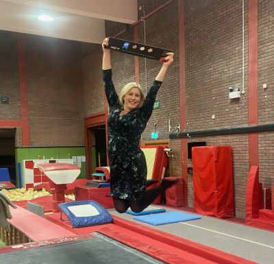 Siwan Davies, Head of Development at Welsh Gymnastics, trampolining while triumphantly holding their new insport Gold plaque.