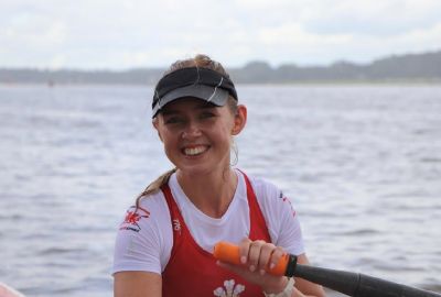 Rebekah in her Welsh Rowing kit, afloat and holding an oar. She is looking at the camera and smiling.