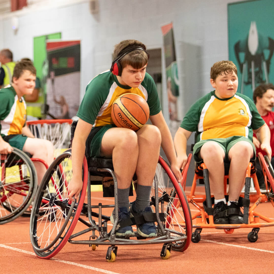 A learner from a Swansea school tries wheelchair basketball. They are wearing ear defenders and have a face of pure concentration.