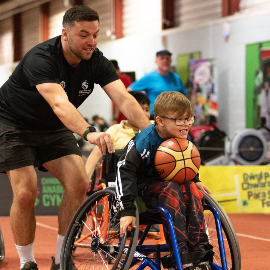 A participant is supported by a coach playing wheelchair basketball