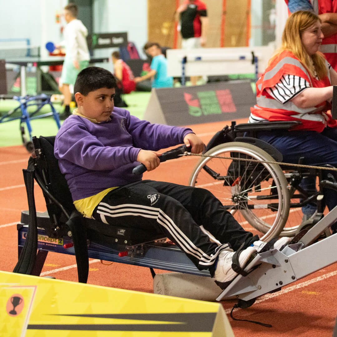 A participant tries adapted rowing. They are using a fixed rowing machine, focused on the data screen.